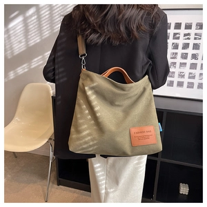 Close-up of olive green canvas tote bag featuring brown leather handles and a fashion patch