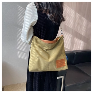 Model wearing a large khaki canvas crossbody bag with leather handles in a minimal interior