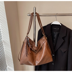 Detailed view of the side drawstring and braided charm on this large brown leather tote bag