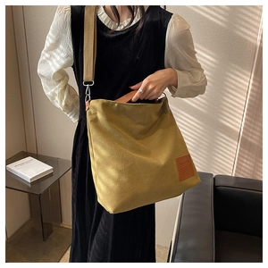 Detailed side view of the mustard yellow canvas tote bag worn by a model in a cozy room