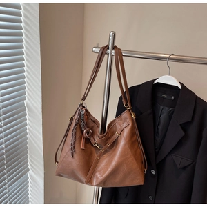 Detail view of a vintage brown leather tote bag with tassels hanging on a hanger