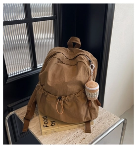Close-up of brown nylon backpack with drawstring pocket and plush doll charm