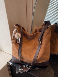 Brown suede tote bag with leather straps and plush charm on a shelf with light shadows