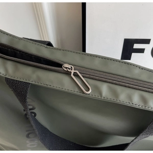 Detailed macro view of dark green tote bag with silver zipper and black woven strap