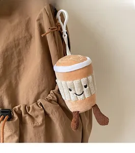 Close-up of a plush coffee cup doll charm with a smiley face hanging on a brown backpack
