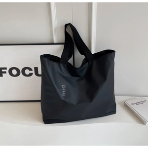 Detail of a black nylon tote bag featuring wide fabric straps and subtle one lettering