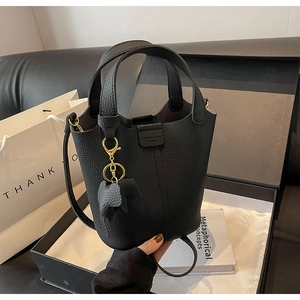 Detail of black pebbled leather bucket bag with top handles and elephant charm in gift box
