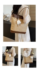Detail view of straw woven tote bag with brown leather trim and fluffy white charm