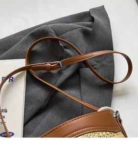 Detail of adjustable brown leather shoulder strap and buckle on woven straw bucket bag