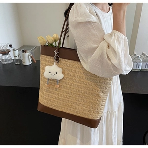 Detail of straw woven tote bag with brown leather handles and a plush cloud charm