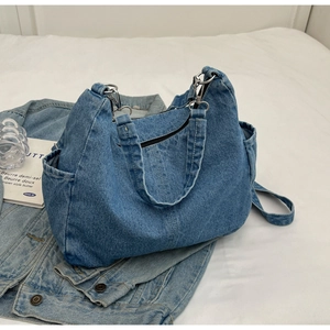 Détail du sac cabas en jean bleu avec boucles argentées et poches latérales sur drap
