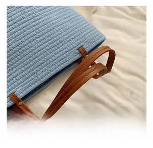Detail of blue straw tote bag showing brown faux leather handle and gold rivet