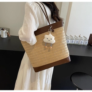 Detail of summer straw tote bag with brown leather handles and a white cloud charm
