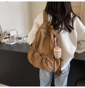 Detail view of brown drawstring nylon backpack with a plush coffee cup pendant