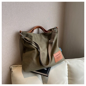 Detailed view of olive green canvas tote bag with brown leather handles on a white sofa