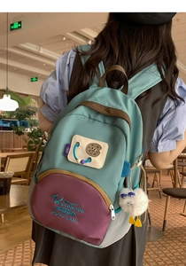 Detailed embroidery and plush pom-pom keychain on a light blue nylon backpack