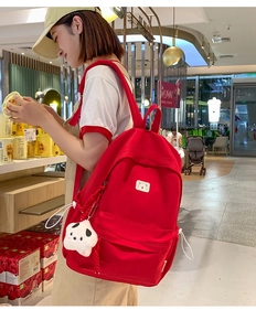 Close-up of red canvas backpack with white bear badge and plush panda accessory