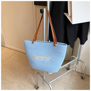 Detail of light blue woven straw tote bag featuring Summer embroidery and leather straps