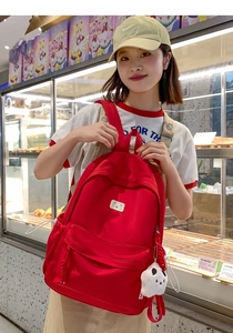 Detail view of large red nylon backpack featuring cute bear patch and plush mascot