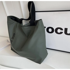 Detail of the dark green waterproof nylon tote bag featuring a black wide canvas strap