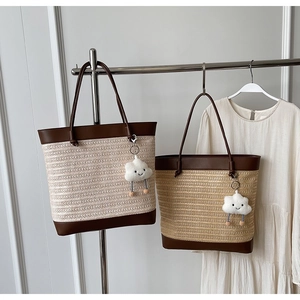 Close-up of woven straw tote bag with brown leather handles and cloud plush charm