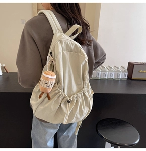 Close-up of a beige nylon backpack featuring a cute coffee cup plush charm accessory