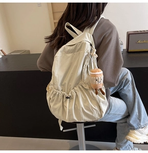 Detail of beige lightweight backpack featuring side drawstring pocket and cute coffee charm