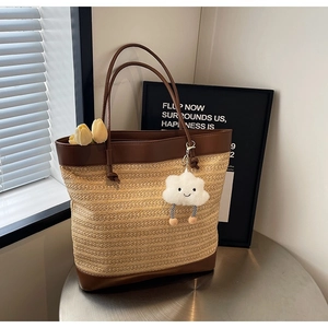 Detail of summer straw tote bag with brown leather trim and fluffy cloud charm