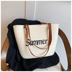 Close-up of beige woven tote bag featuring black Summer embroidery and brown leather straps