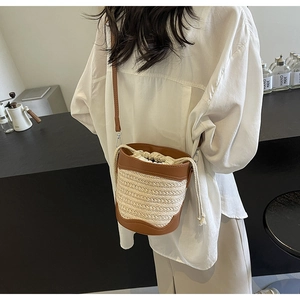 Detailed view of the woven straw bucket bag with brown leather trim and drawstring closure