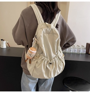 Detail of beige nylon backpack featuring side drawstring and cute brown plush charm