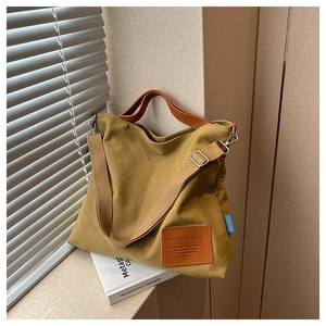Close-up of mustard yellow canvas tote bag with leather straps and logo patch