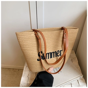 Close-up of beige straw tote bag featuring brown faux leather straps and Summer embroidery
