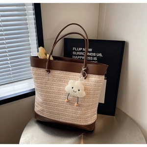 Detail of woven straw tote bag with brown leather trim and cute white cloud charm