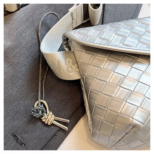 Detalle de bolso bandolera de cuero trenzado plateado con nudo metálico y correa con relieve