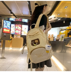 Detail view of cream canvas backpack with cute plush charm and embroidery accents