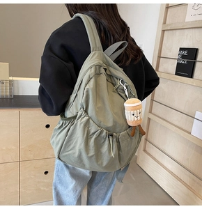 Sage green nylon backpack featuring a large drawstring pocket and a plush coffee charm