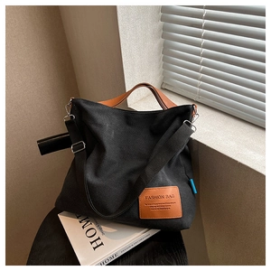 Detail of black canvas tote featuring brown leather handles and fashion logo patch