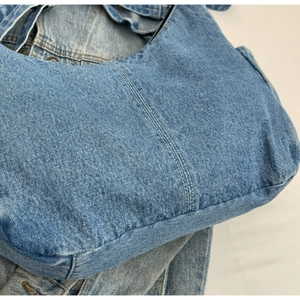 Détail du sac hobo en jean bleu clair montrant la double couture blanche et le tissu