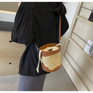 Detail of straw bucket bag featuring brown leather trim and beige drawstring closure