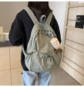 Detail of olive green nylon backpack featuring a cute coffee cup plush charm and drawstring
