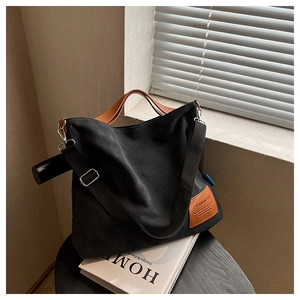 Detail of black canvas tote bag showing fashion tag and leather handle with metal hooks
