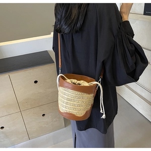 Detail of straw bucket bag with brown leather trim and drawstring closure on a model
