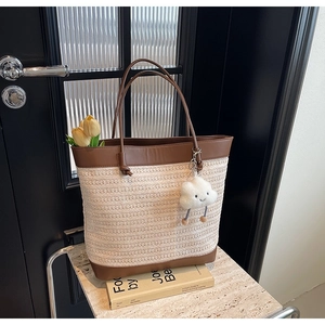 Minimalist straw tote bag with brown leather handles and plush cloud charm for summer commute