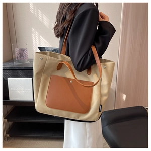 Detail of beige canvas tote bag showing dark brown leather pocket and metal side buckle
