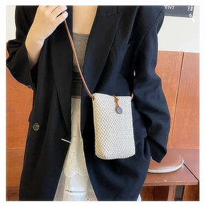 Detail showing woven straw texture and brown leather strap on minimalist crossbody bag