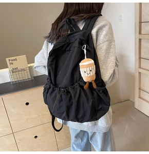 Detail of black nylon backpack with side drawstring pocket and cute coffee plush charm