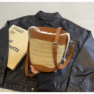 Detail of a color-block straw bucket bag featuring a brown leather handle and drawstring liner