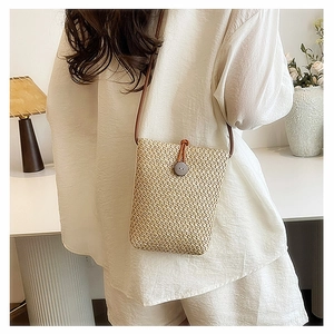 Detail of woven straw crossbody bag with brown strap and wooden button closure