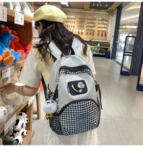 Detailed view of lightweight backpack with plaid patchwork and plush ball pendant charm